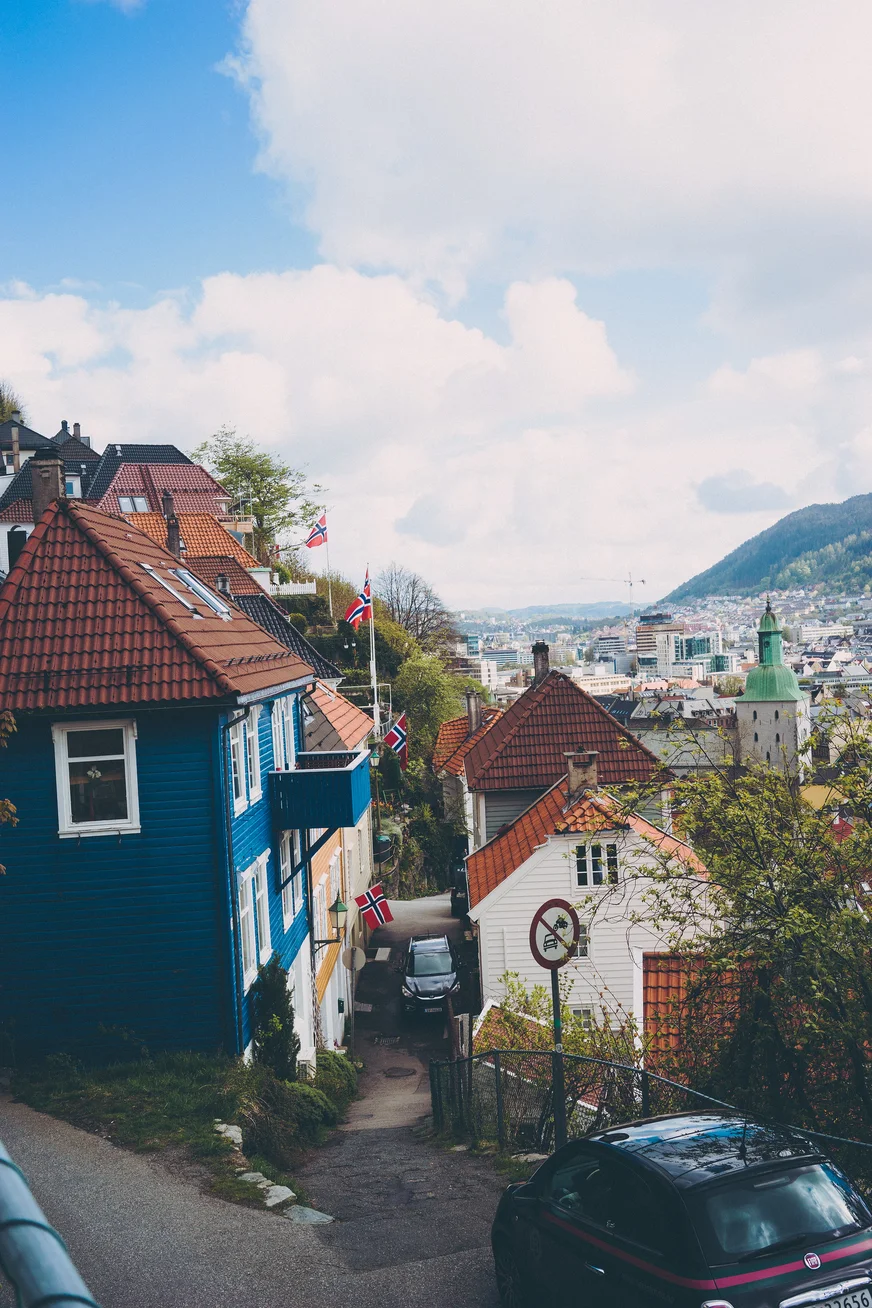 A steep lane between colorful wooden houses overlooking a city and mountains